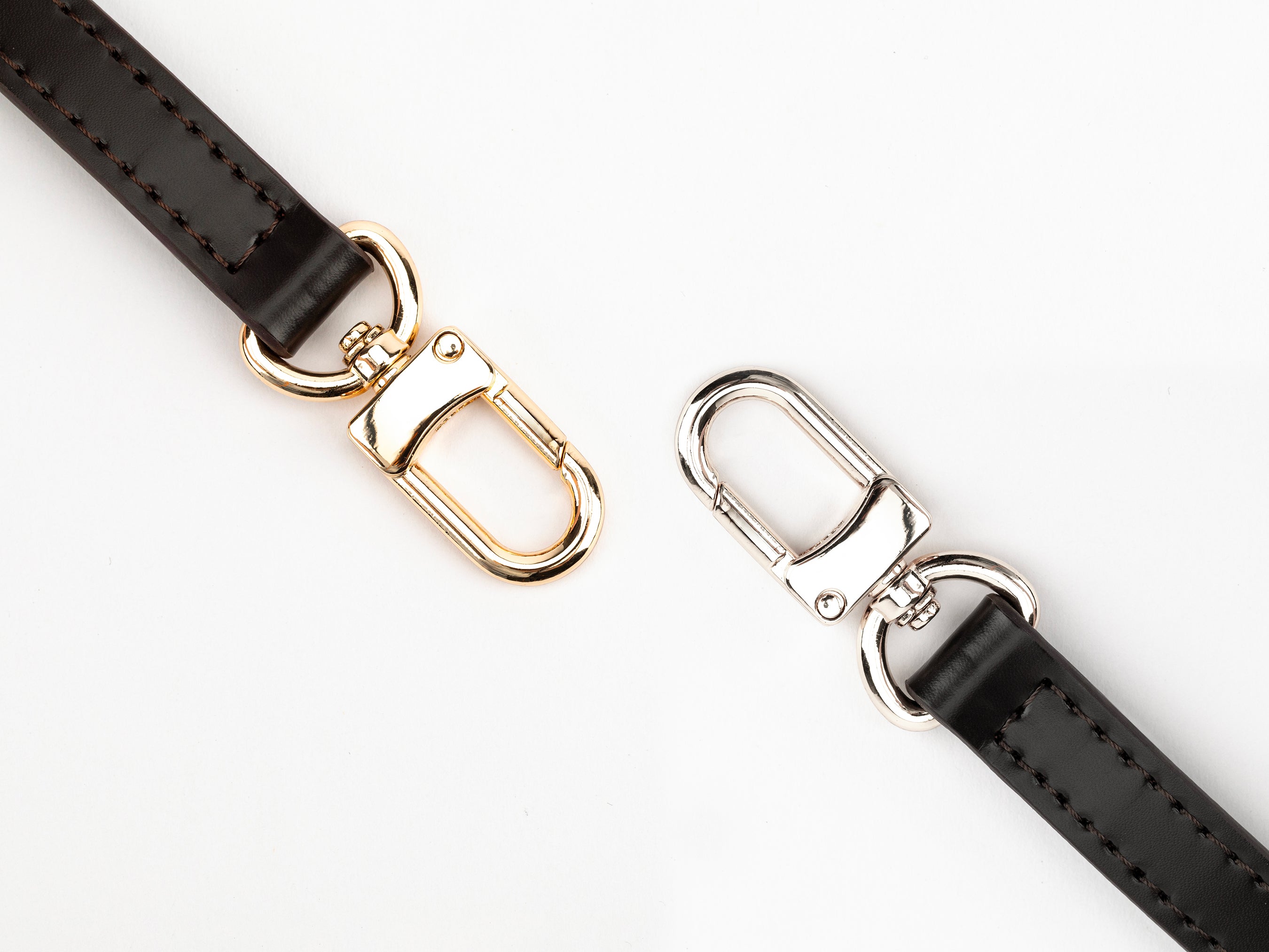 Two black leather straps with gold and silver metal clasps on a white background