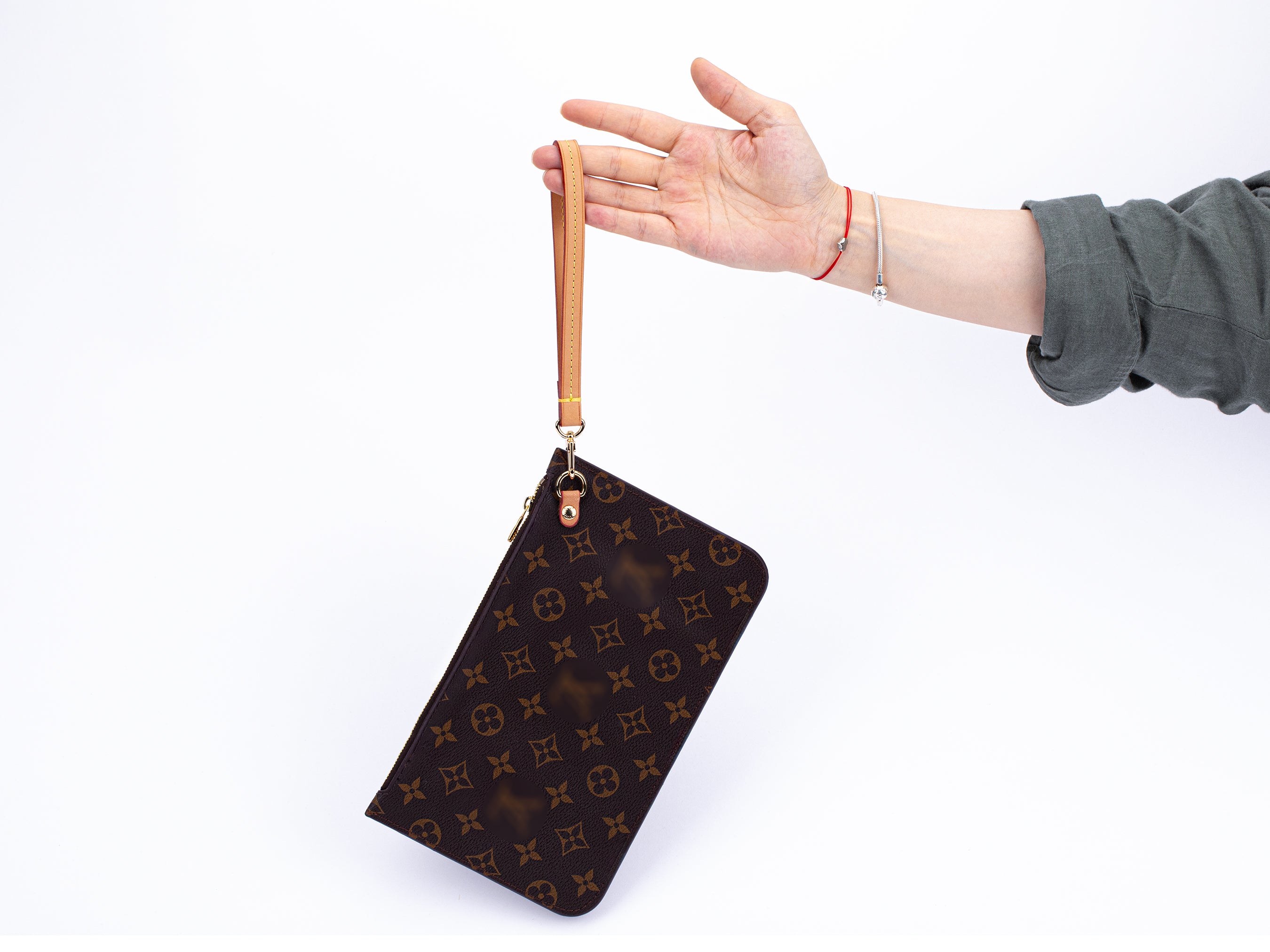 A person's hand holding a brown clutch bag attached to a wristlet strap.